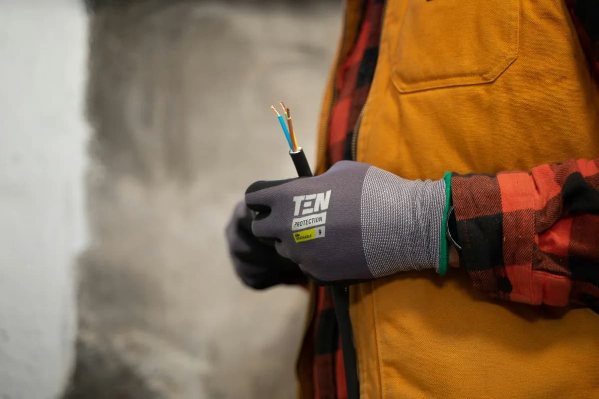Eletricista com luva de proteção manuseando fiação elétrica.